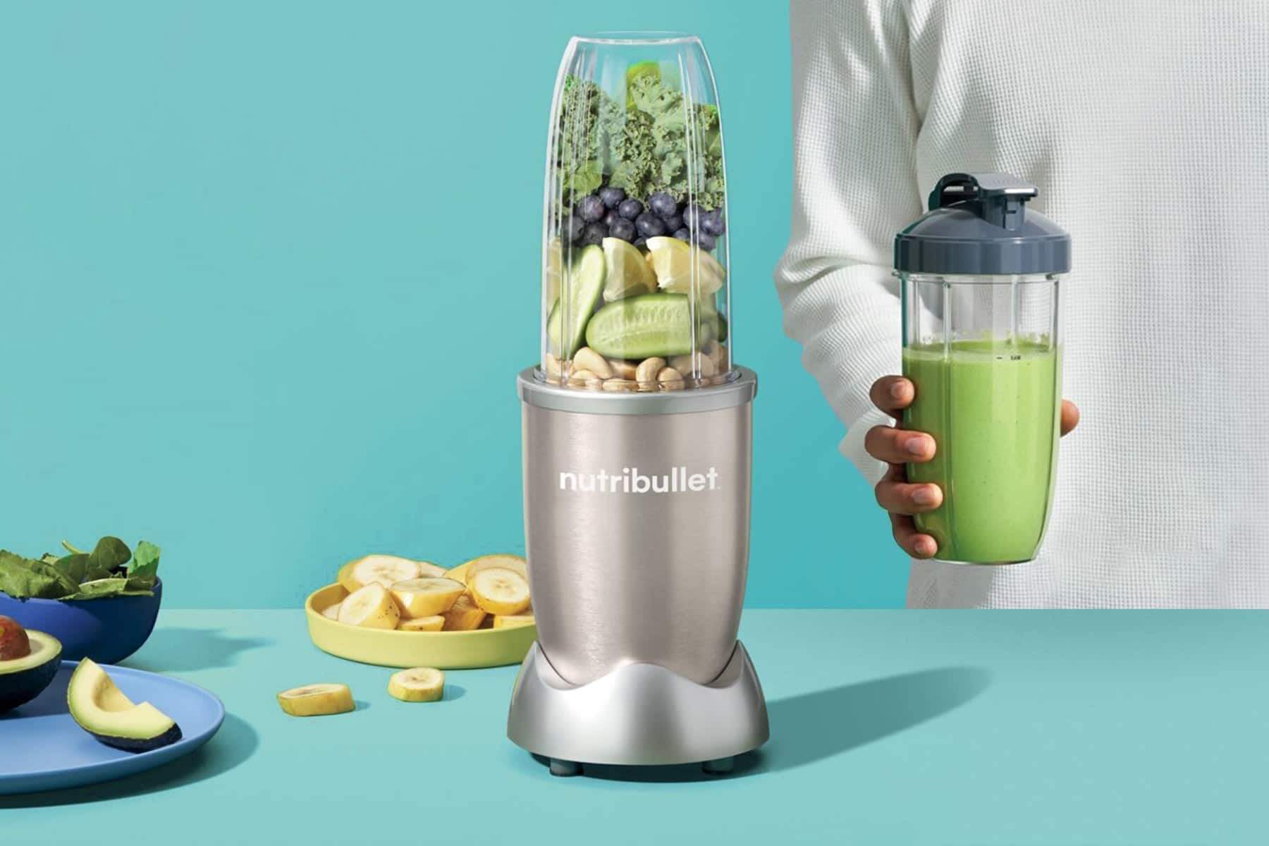 uprostřed grafiky stojí mixér Nutribuller, po jeho levé straně leží ovoce a zelenina, po pravé straně stojí muž držící hotové smoothie. Pozadí je modré, chladné