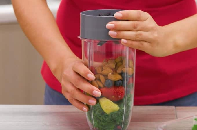 Hands securing cup filled with fruit to blade